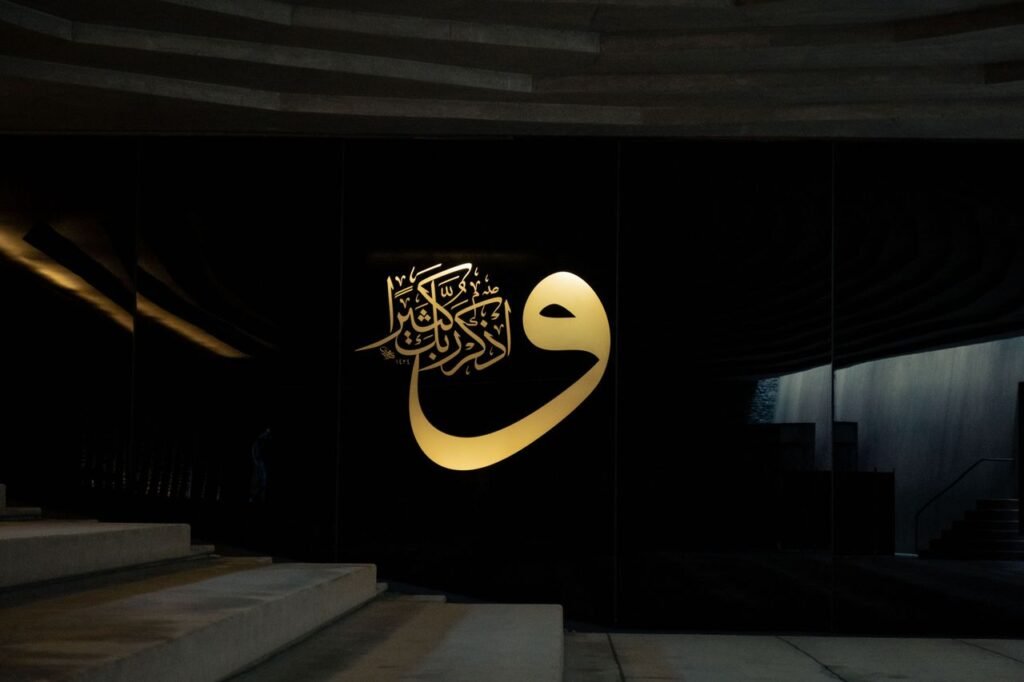 Elegant Islamic calligraphy in gold on a modern black wall, featuring architectural elements and stairs.