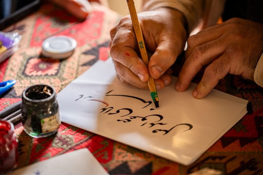 Hands writing traditional calligraphy with a pen on paper, showcasing cultural artistry in Baku.